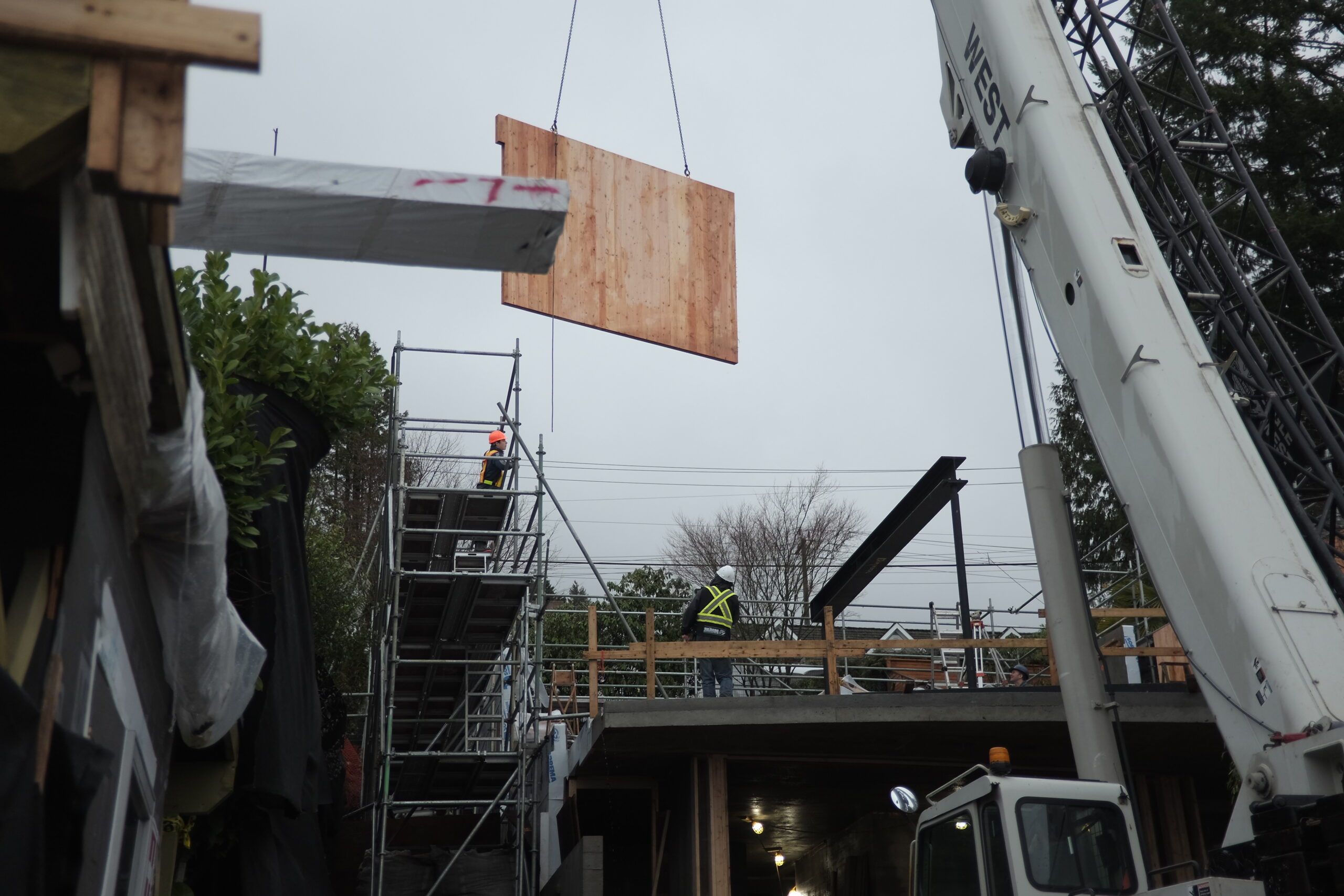 A large CLT wood panel dangles by chains above a project site