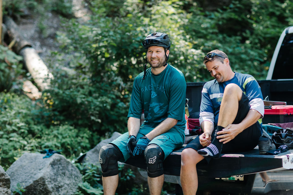 Two mountain bikers sit on a truck tailgate