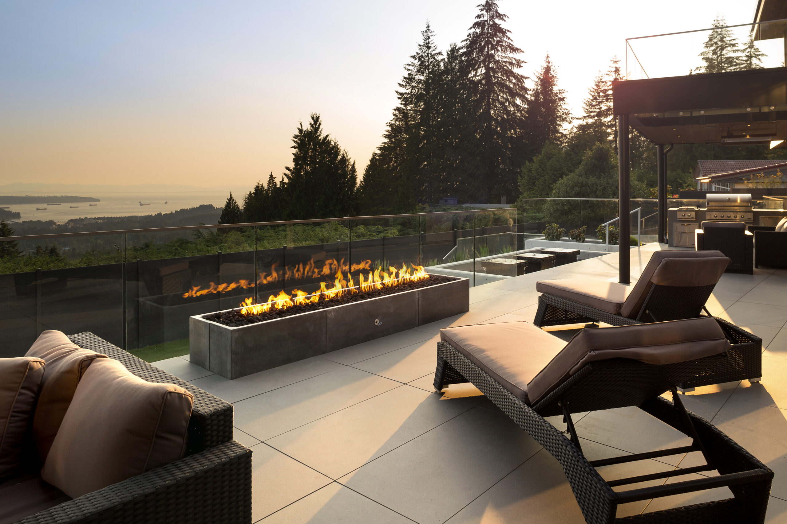 Patio furniture faces a linear fireplace and expansive ocean views