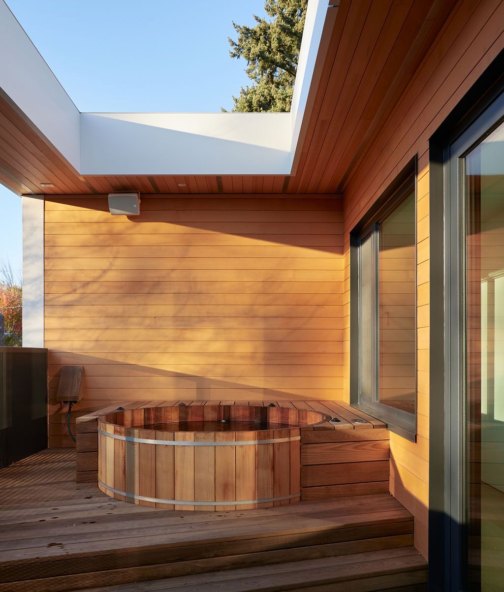 Sunlight shines on a wooden hot tub built into a custom home balcony.