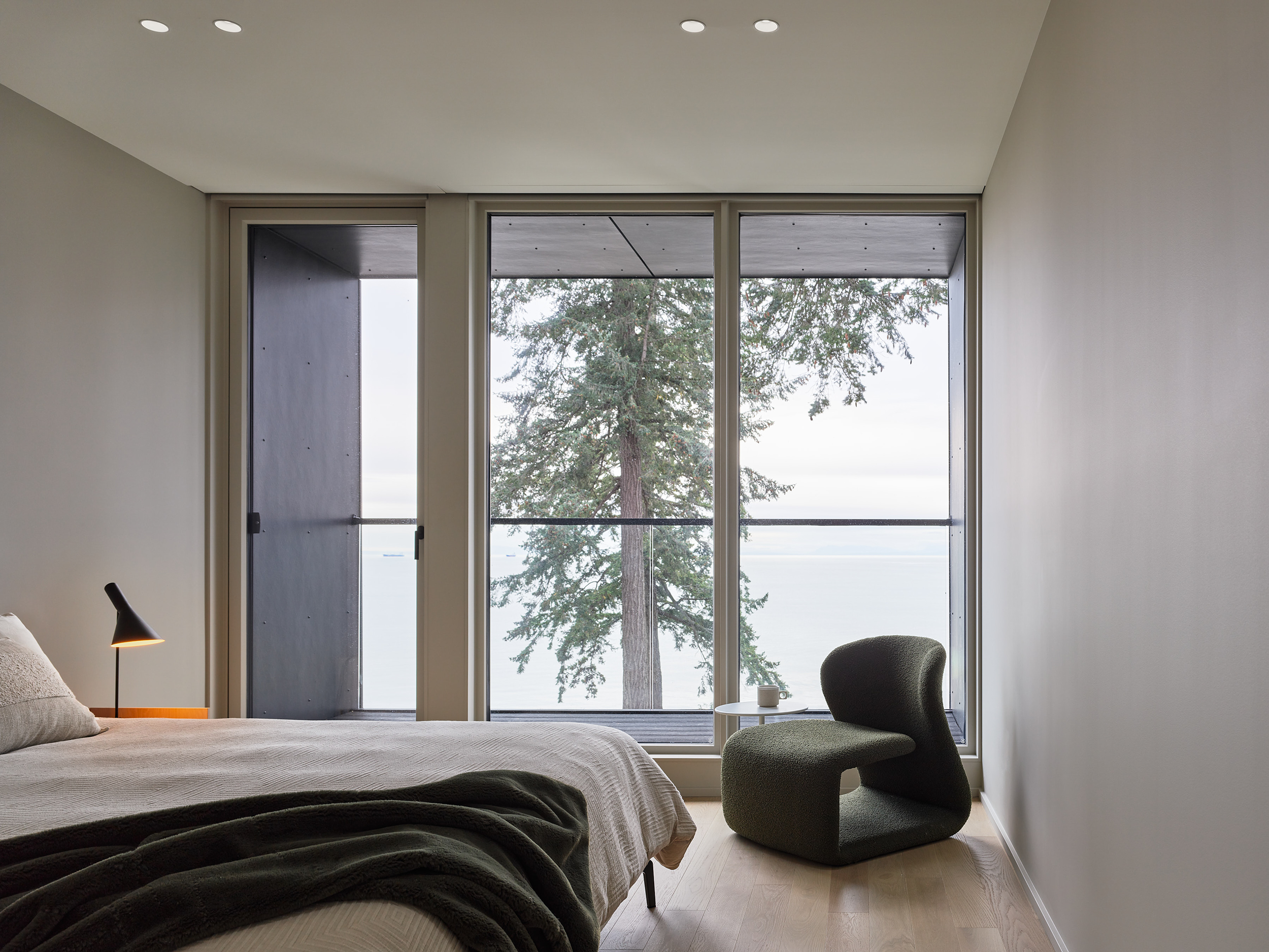 Minimalist bedroom with large floor-to-ceiling windows overlooking ocean and forest landscape