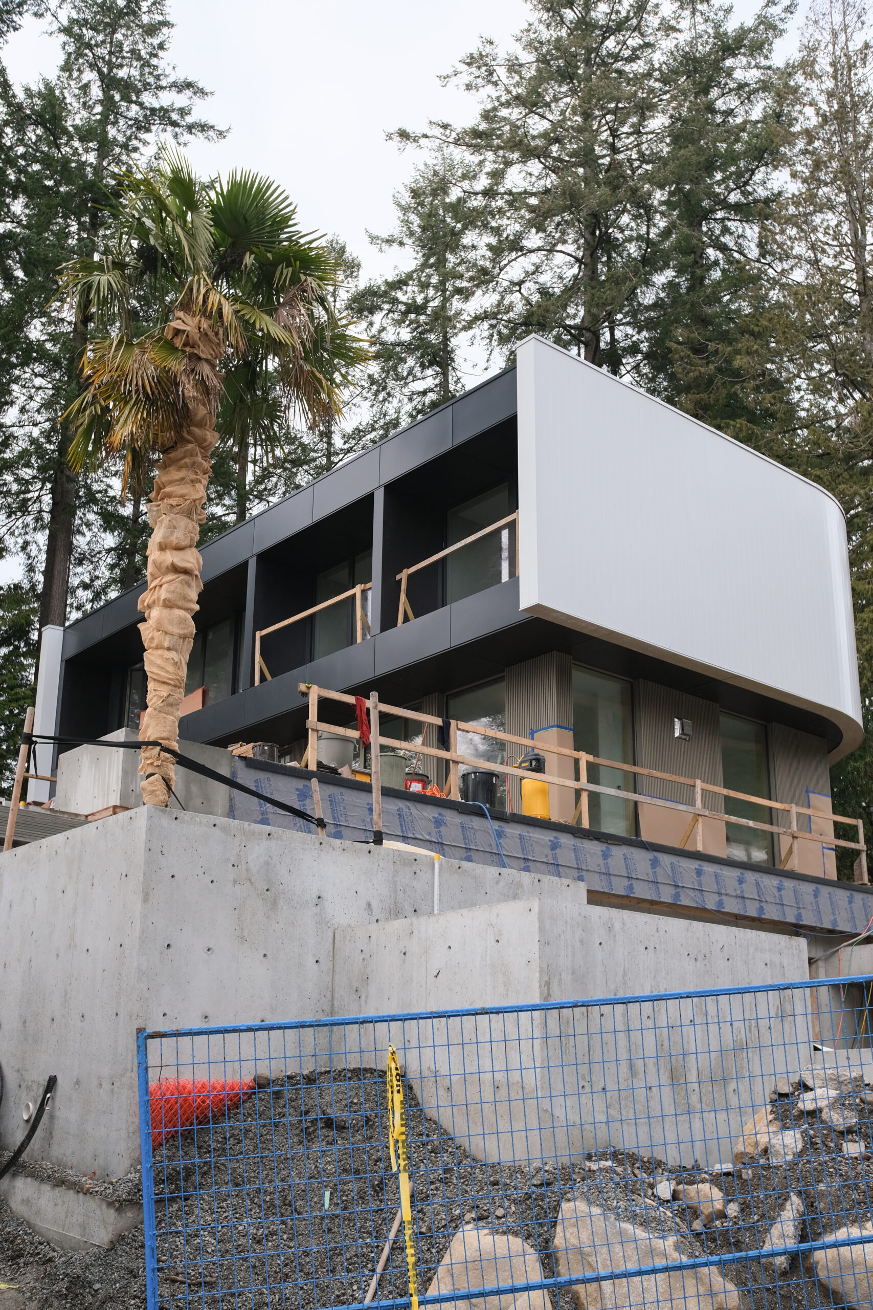 Contemporary custom home under construction with large overhang and concrete retaining wall