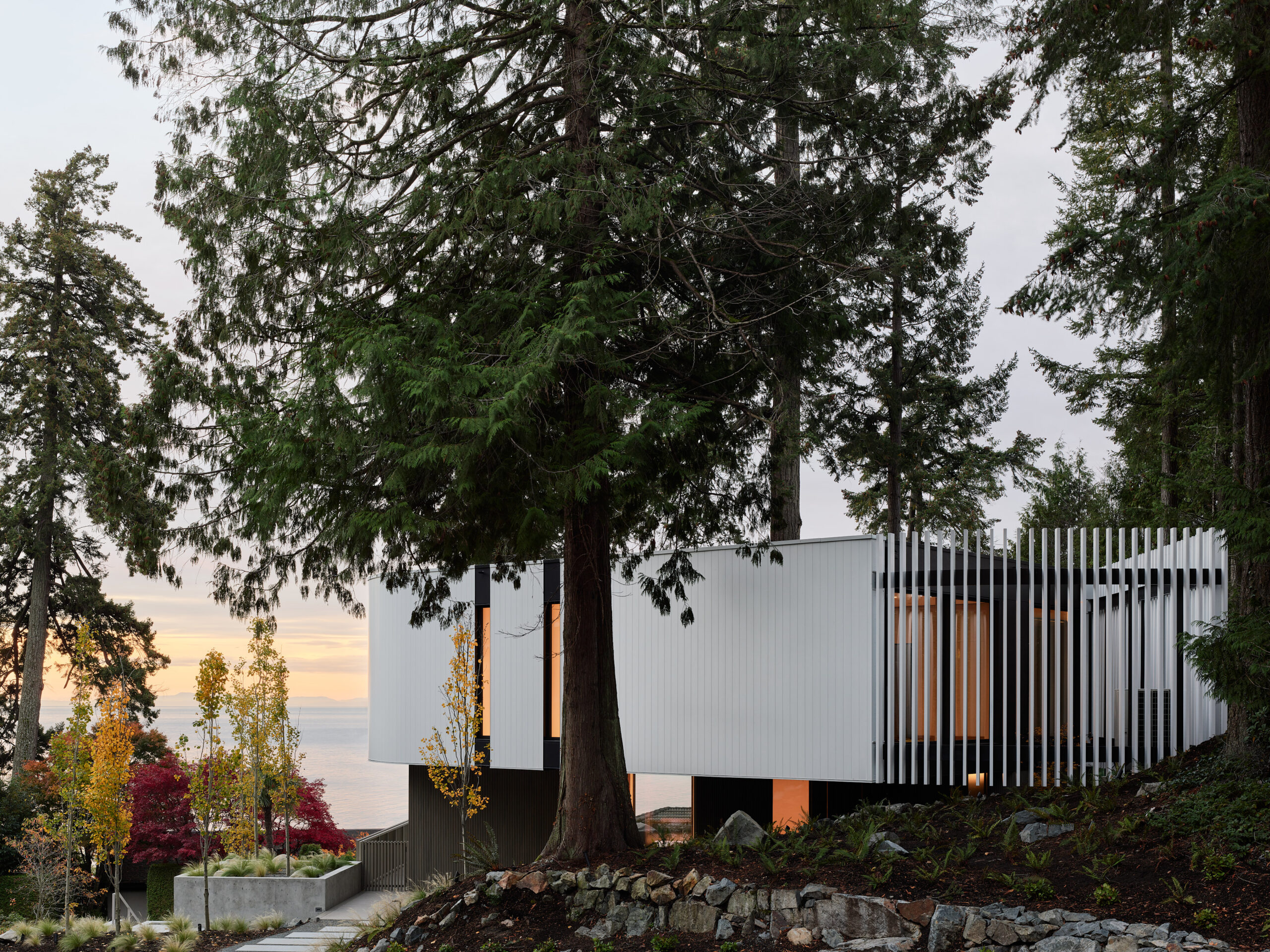 Contemporary custom hillside home with white cantilevered upper level overlooking the ocean and forest landscape