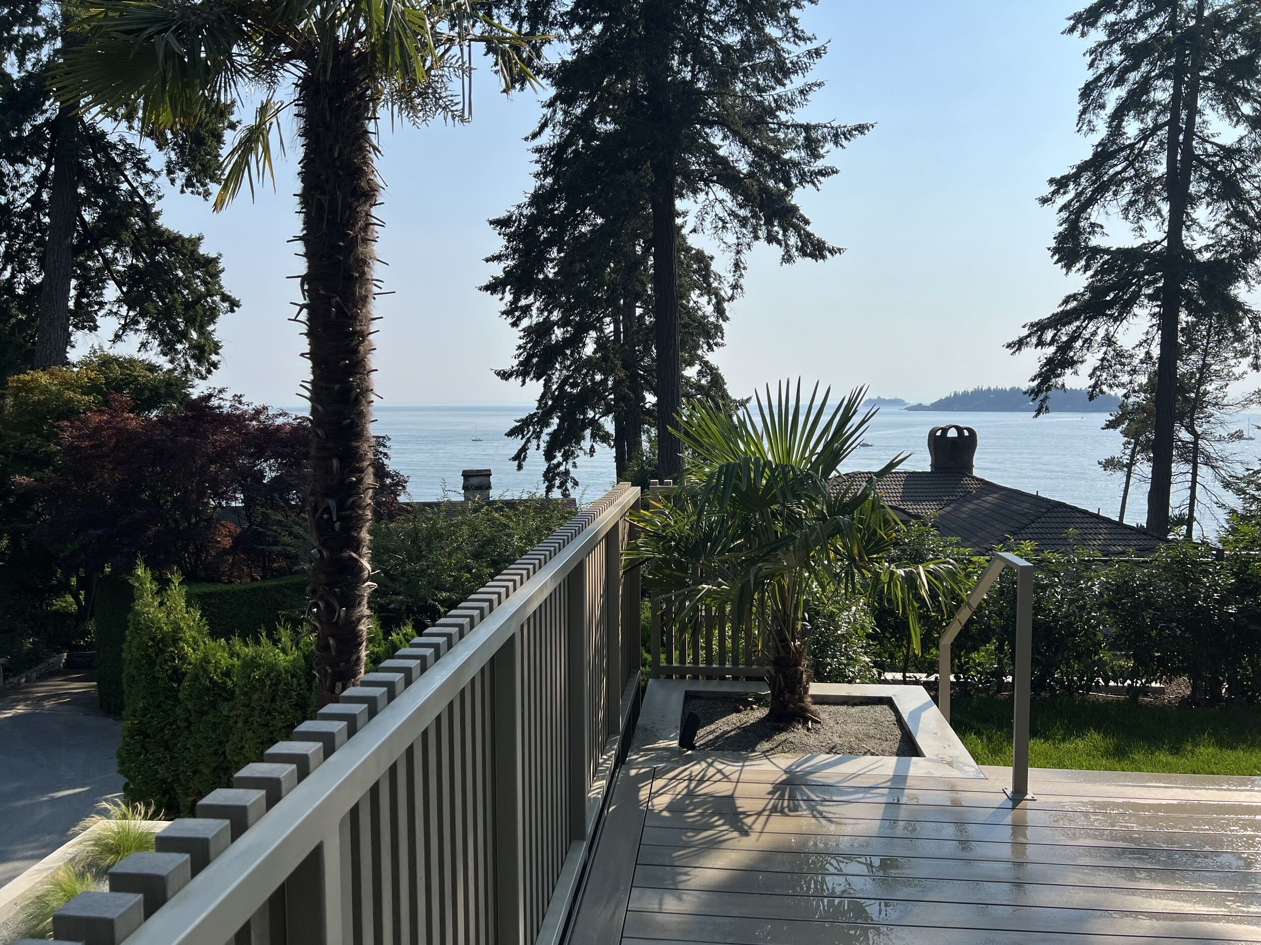 Ocean view from modern custom home terrace surrounded by mature trees and coastal landscape