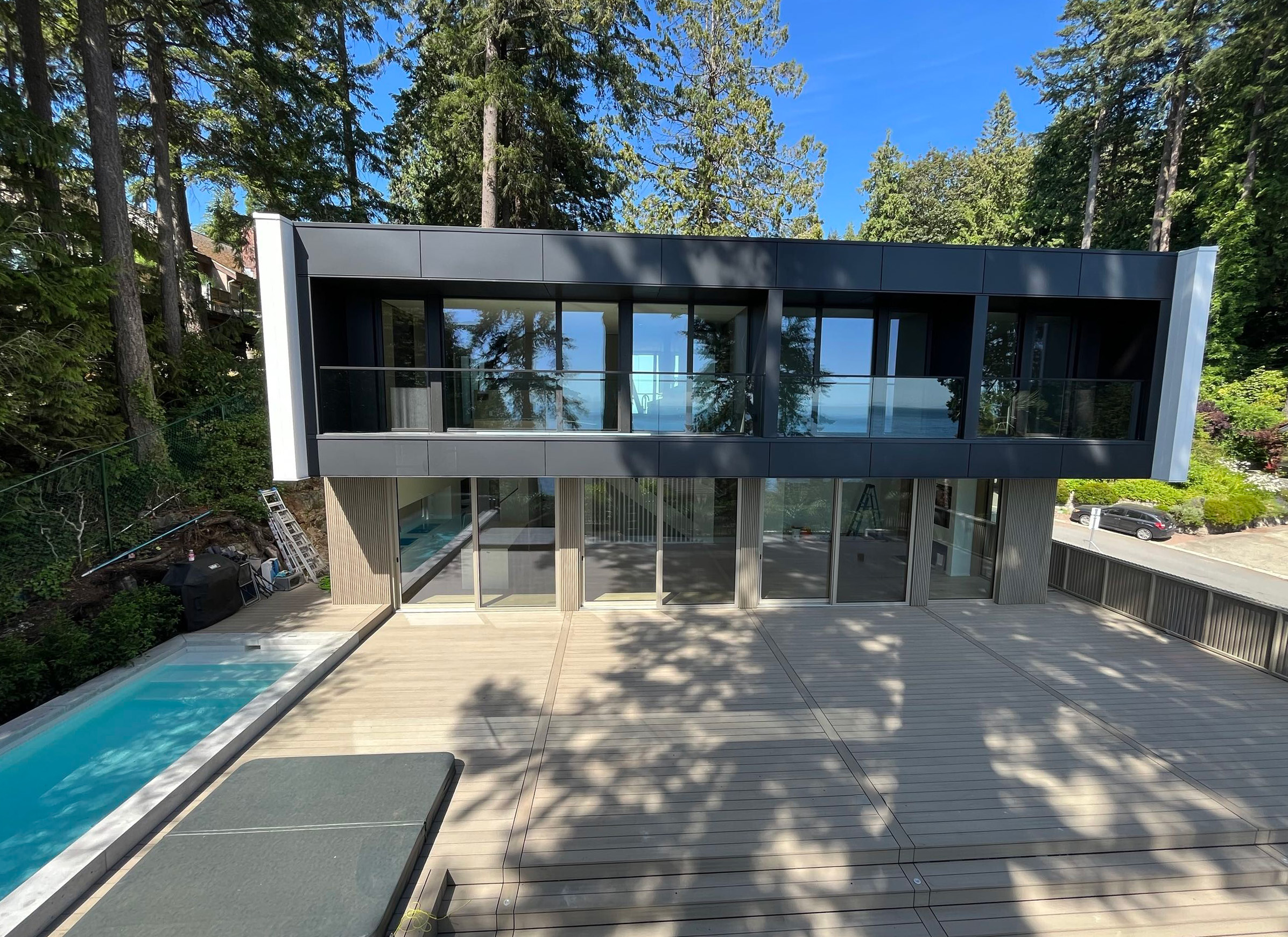 Contemporary hillside home with large glass facade, balcony, and outdoor pool surrounded by forest trees