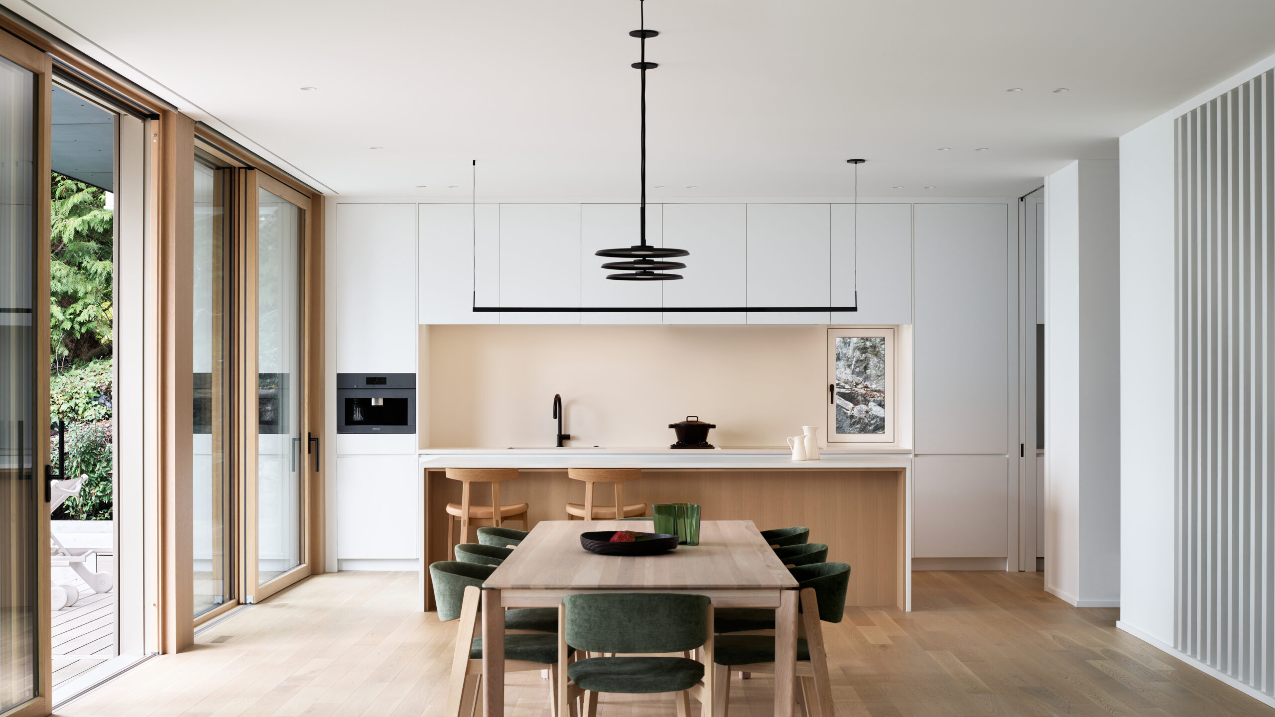 Minimalist modern kitchen and dining area with white cabinetry, wood island, and large windows