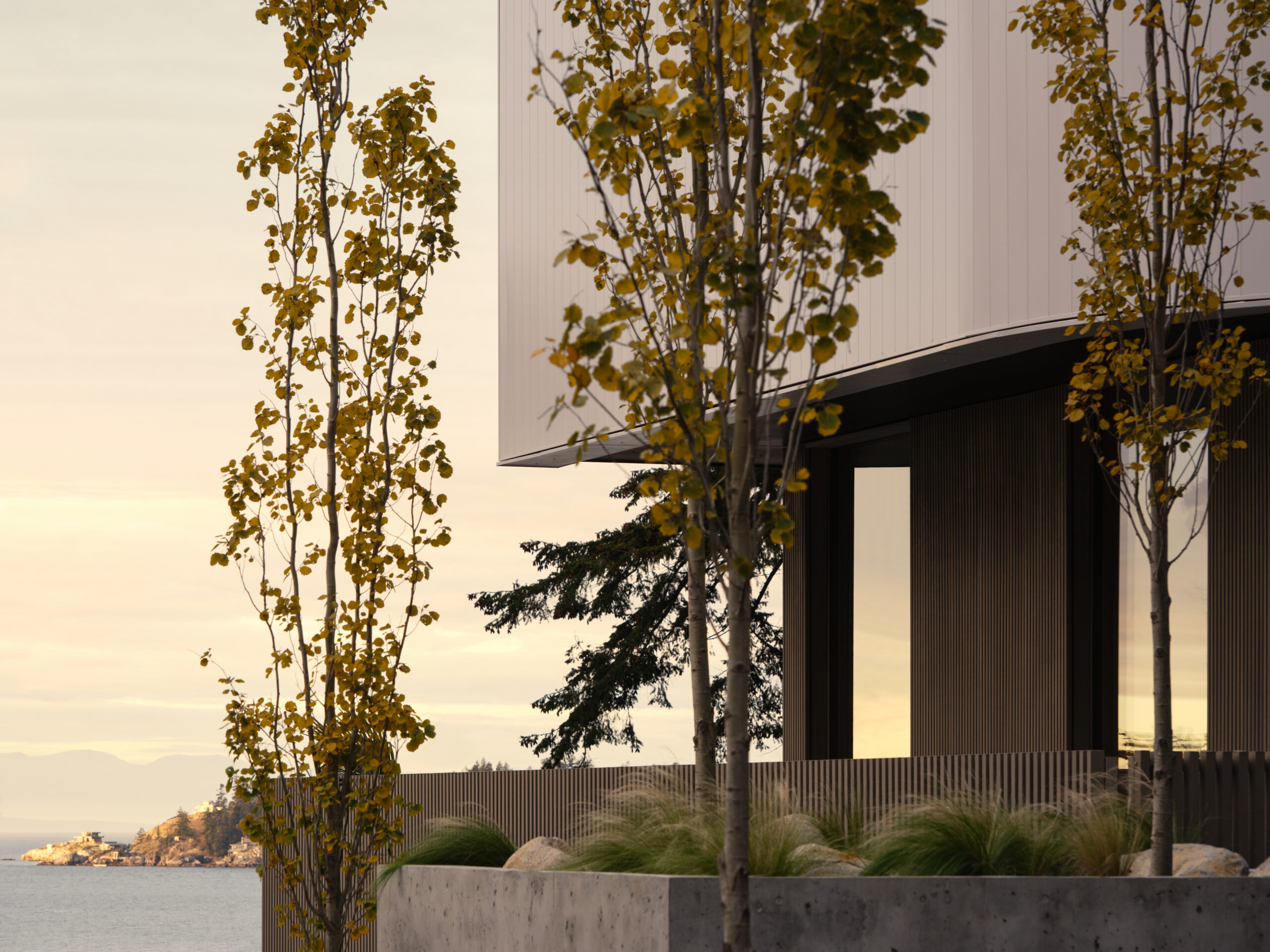 Detail of contemporary custom home exterior with white cladding, landscaped concrete planter, and ocean view